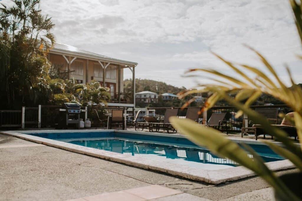 The outdoor swimming pool, surrounded by lounge chairs and palm plants, offers a taste of the relaxing St. John USVI activities. Enjoy a barbecue grill with the backdrop of a charming house under a cloudy sky—an ideal thing to do in St. John U.S. Virgin Islands.