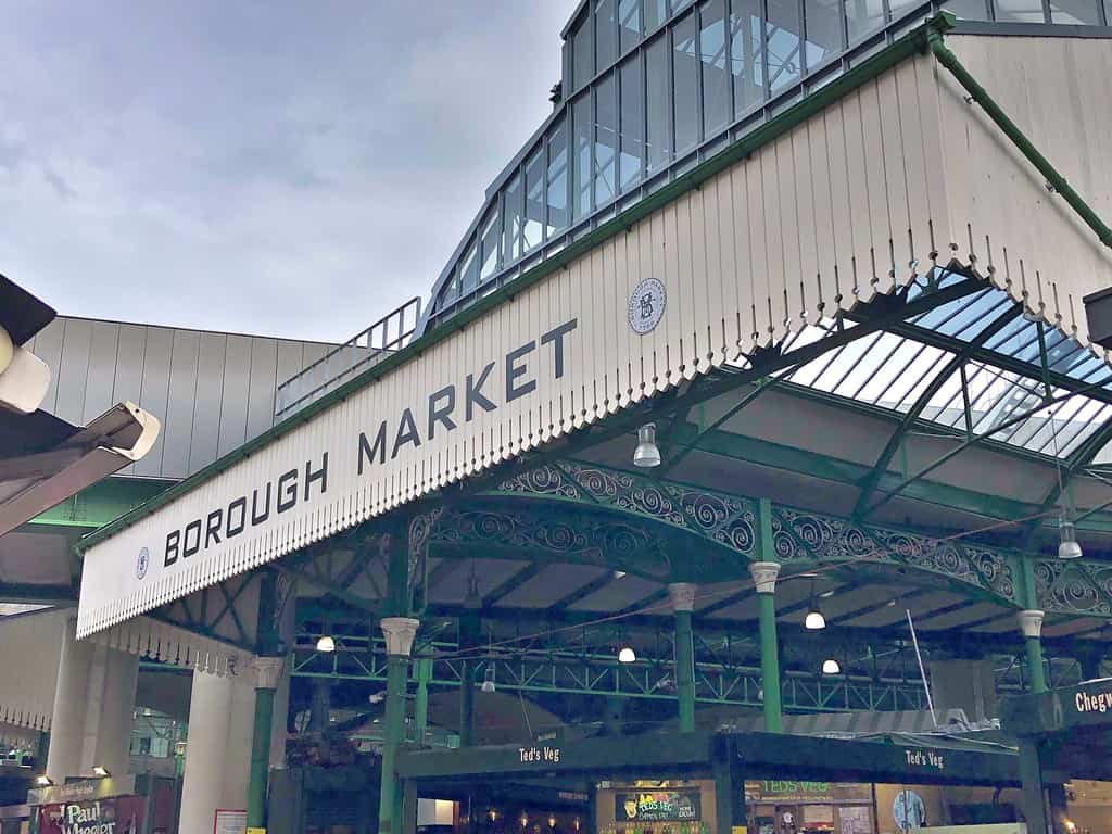 Exterior view of Borough Market, showcasing glass roof and green metal framework with signage for "Ted’s Veg" on the lower level.