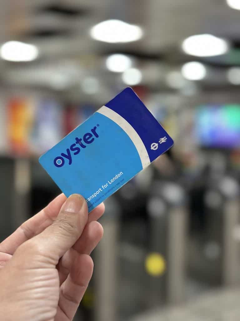 Close-up of a hand holding an Oyster card with the Transport for London logo, blurred background of a subway station.