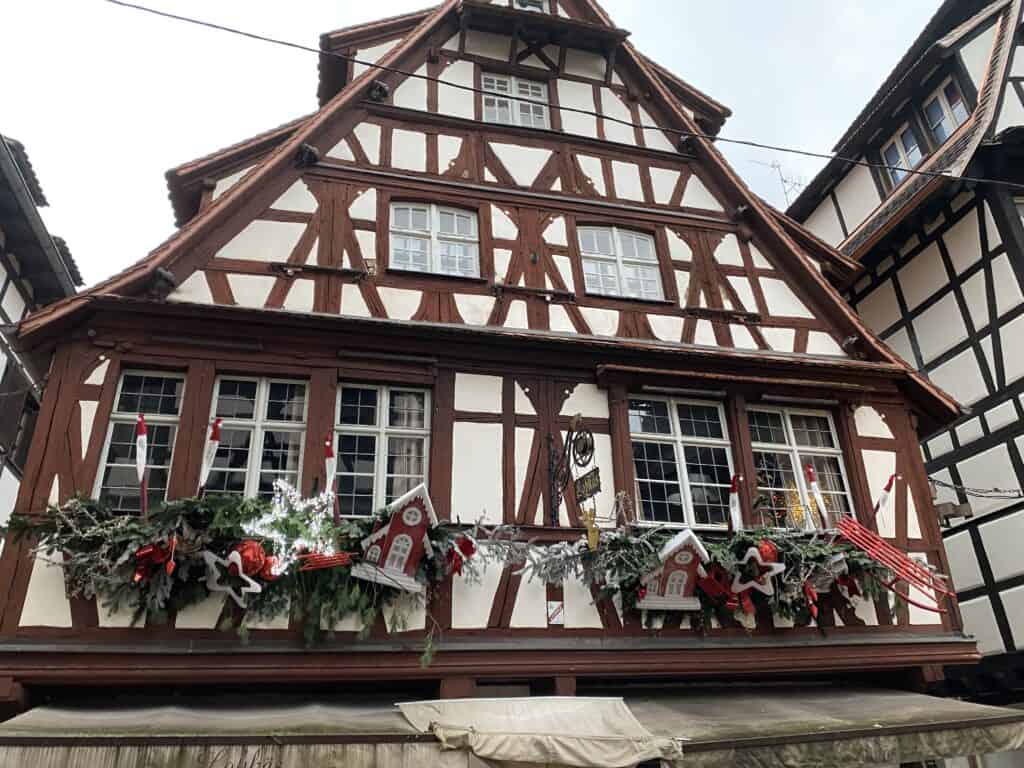 Traditional half-timbered house adorned with festive Christmas decorations, including wreaths, ribbons, and a garland featuring miniature houses