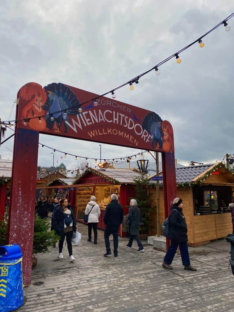 The Welcome sing to the Wienachtsdorf Market with the rustic chalets in the background.