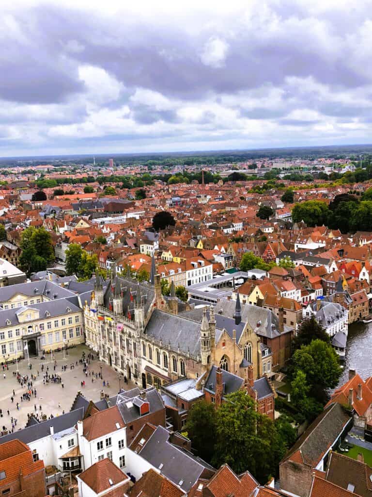 Aerial view of Bruges with historic architecture, showing dense clusters of buildings and a meandering river.