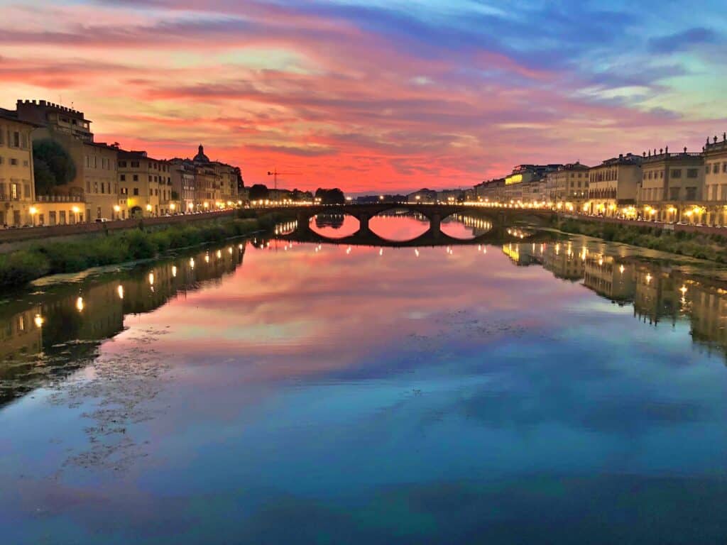 Sunset over ARNO river with reflections, highlighting a bridge and buildings lining the embankments.