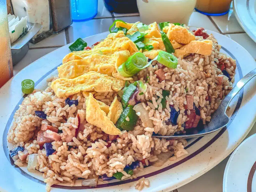 A plate of fried rice topped with scrambled eggs and green onions, with a spoon placed on the side.