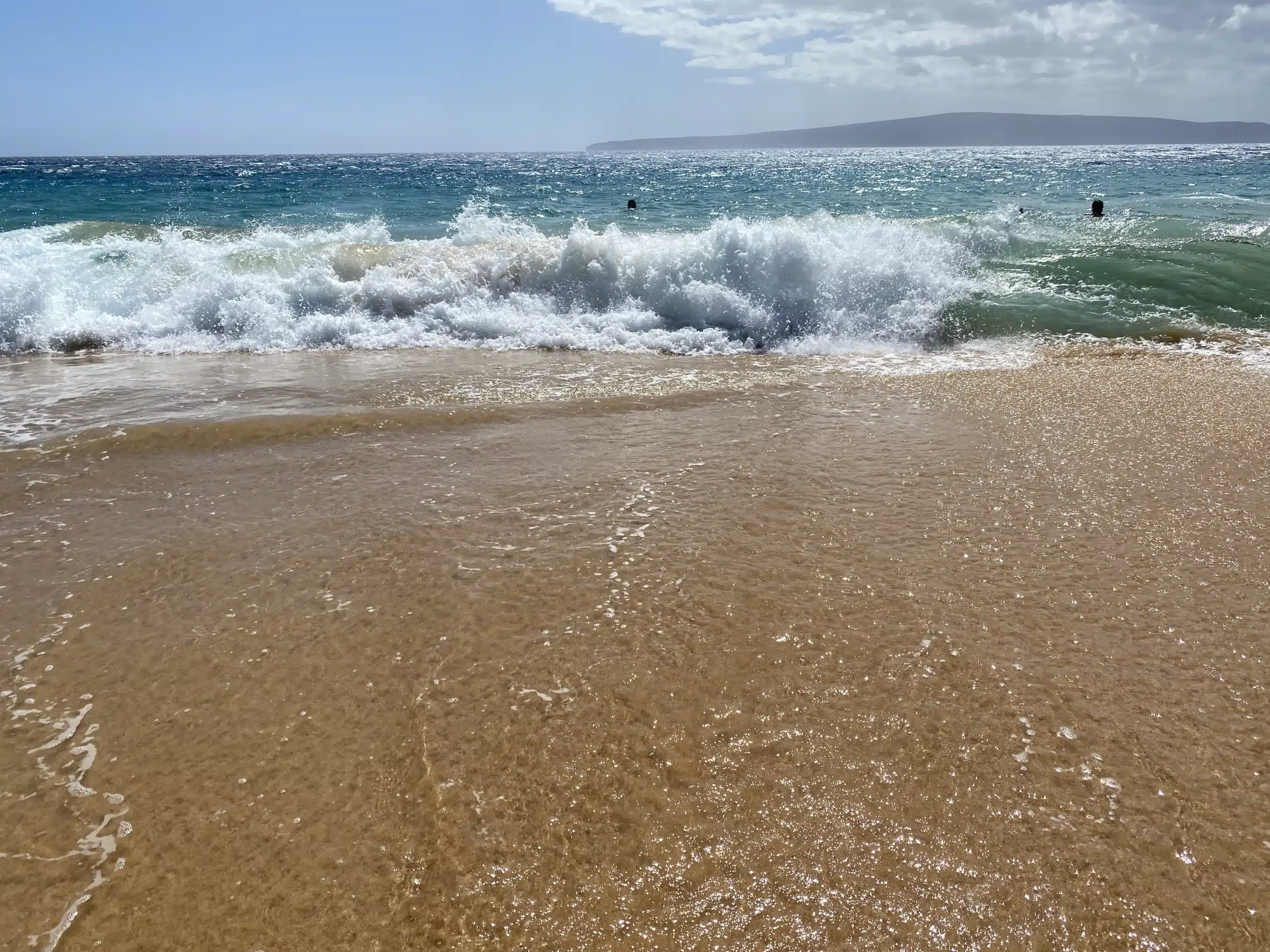 A beach scene showing waves crashing onto the shore under a clear blue sky, with distant land visible on the horizon. Perfect 3- day Maui Beach Itinerary