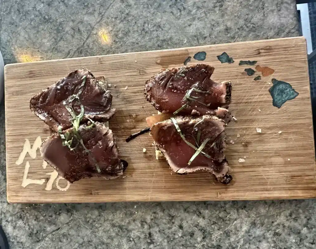 Four pieces of seared tuna garnished with herbs on a wooden cutting board.