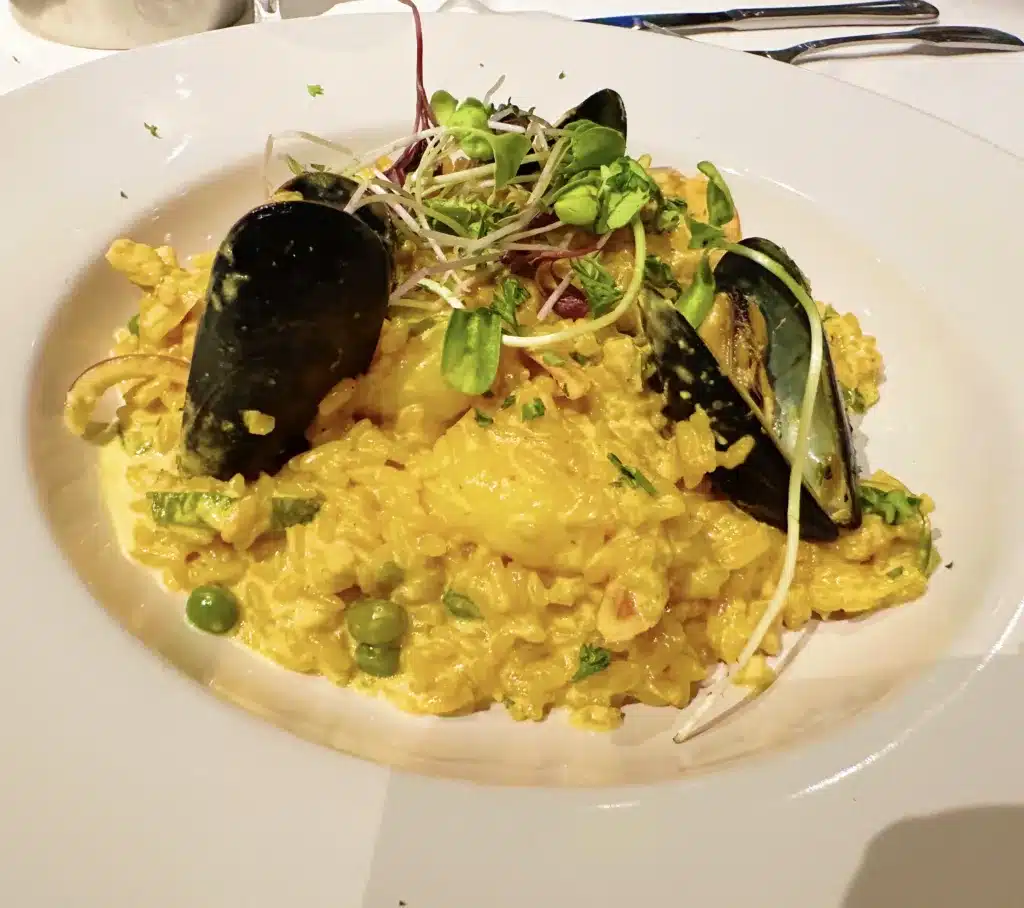 A plate of yellow saffron risotto topped with mussels, microgreens, and peas, garnished with parsley.
