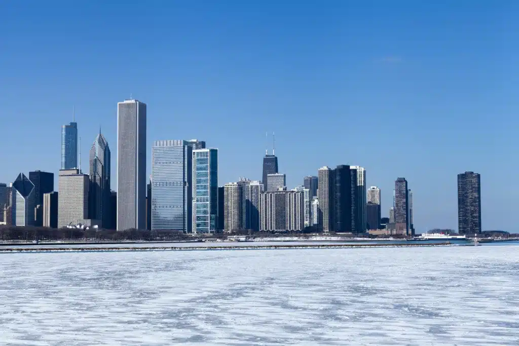 Chicago skyline with tall buildings along the lakefront on a clear blue day, with ice covering the water.