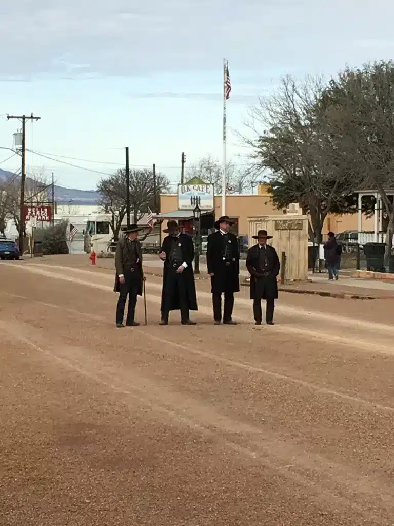 Four people in period clothing stand on a dirt street with historic buildings and trees in the background, reminiscent of scenes from popular day trips from Tucson.