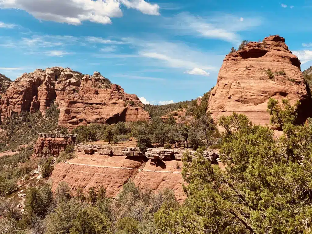 Explore the desert landscape on day trips from Tucson, where you'll find striking red rock formations, vibrant green vegetation, and a pristine blue sky dotted with scattered clouds.