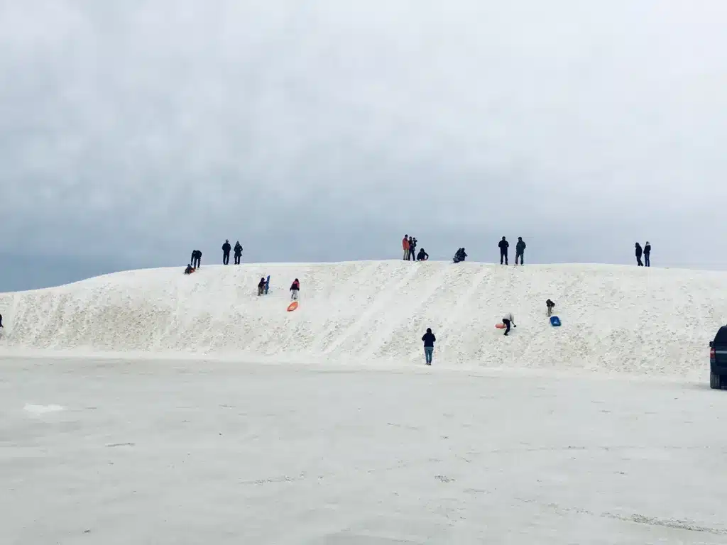 A favorite spot for day trips from Tucson, people stand and play on a large, white sand dune under a cloudy sky.