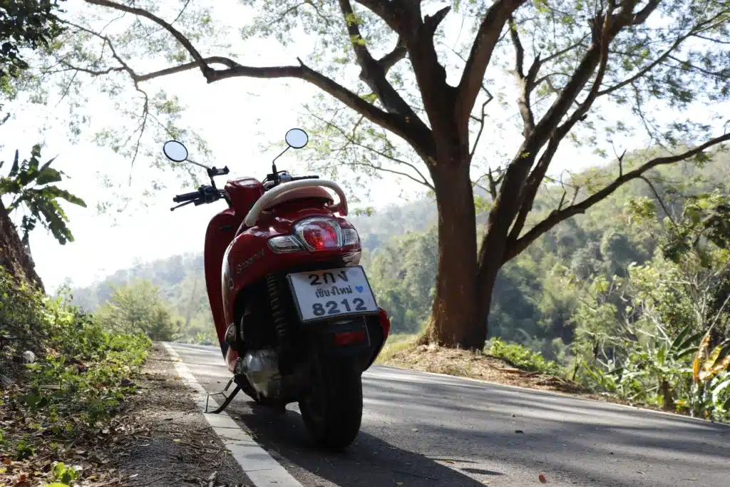 Red scooter parked on a roadside with a scenic backdrop of hills and trees.Thailand. Chiang Mai.
