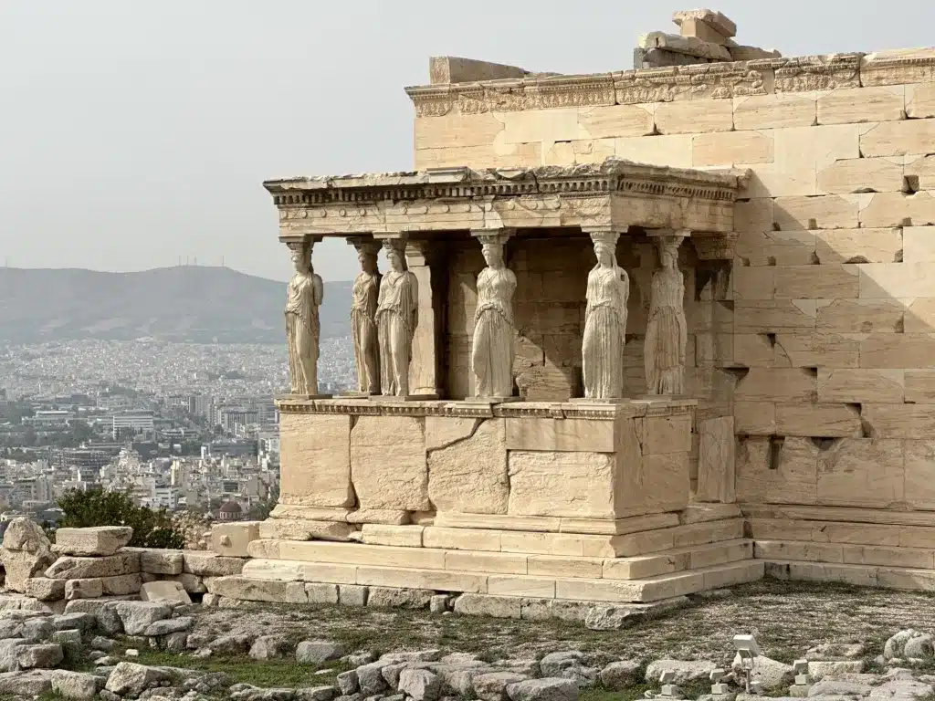 Experience a breathtaking view of the Erechtheion with Caryatids on the Acropolis in Athens, Greece, reminiscent of a Virgin Voyages Cruise adventure, as it overlooks the vibrant cityscape below.