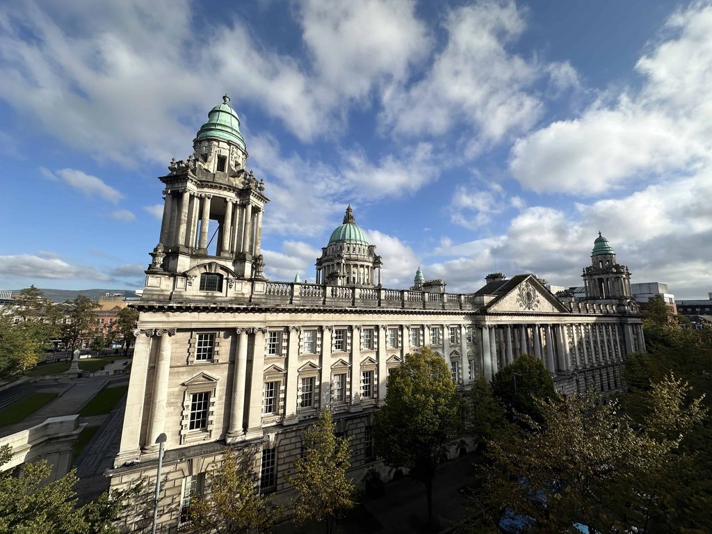 Belfast City Hall, a grand stone building with green domed towers, under a blue sky; it is one of the best things to do in Belfast.