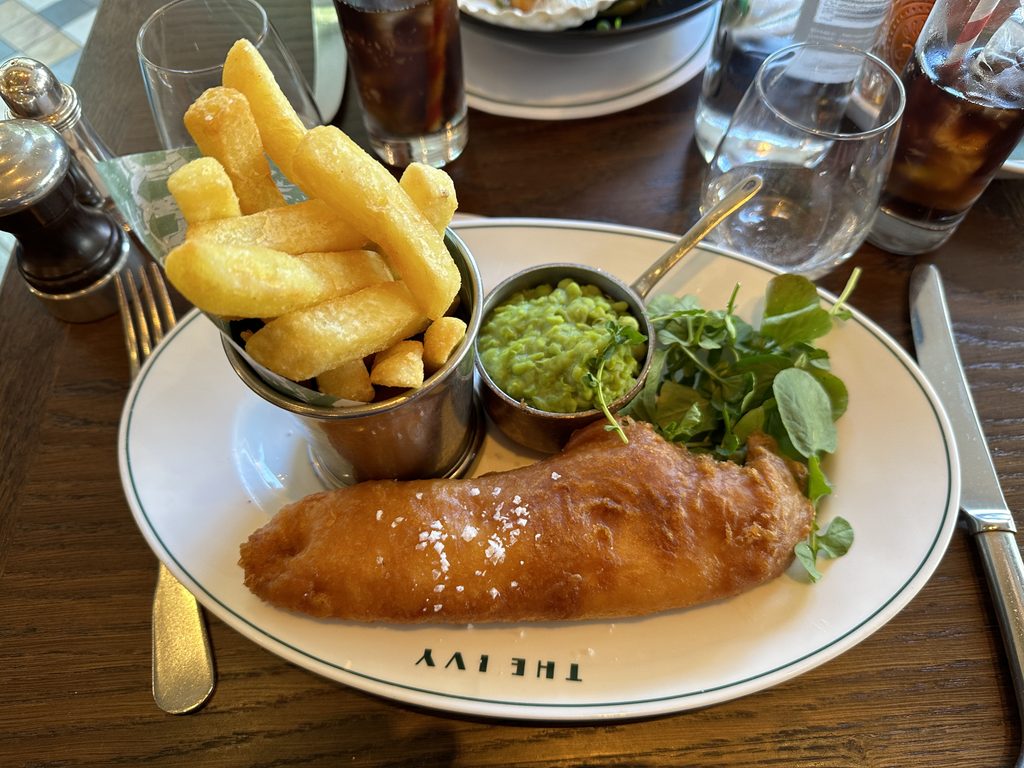 Fish and chips with mushy peas and a side salad on a plate branded with The Ivy logo, a highlight among the best things to do in Belfast.