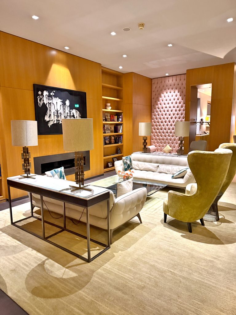 A modern hotel lobby lounge with light-colored sofas, high-backed armchairs, and wood-paneled walls, perfect for relaxing after the best things to do in Belfast.