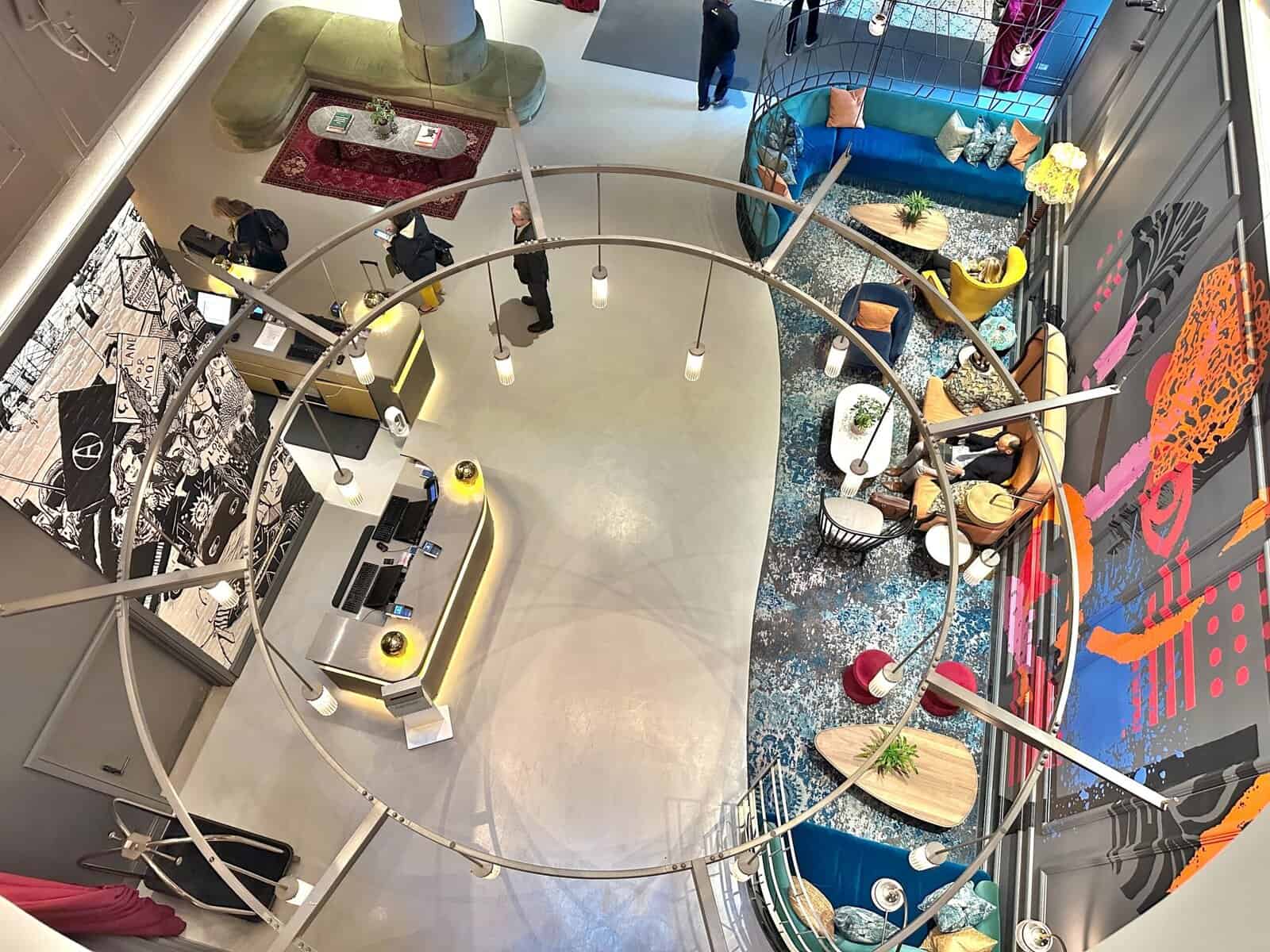 High-angle view of the Andaz London Liverpool Street lobby, featuring a circular pendant light fixture, a reception desk, and various seating areas.