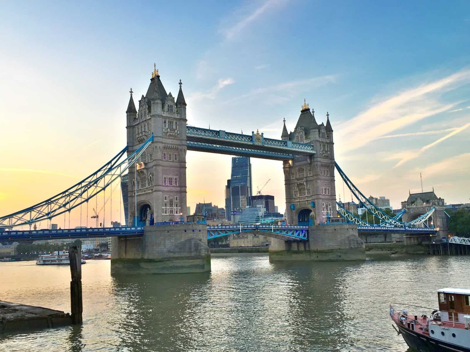 Tower Bridge in London at sunset, captured in a beginner's guide to the city, with the River Thames gracing the foreground and iconic city buildings illuminated in the background.