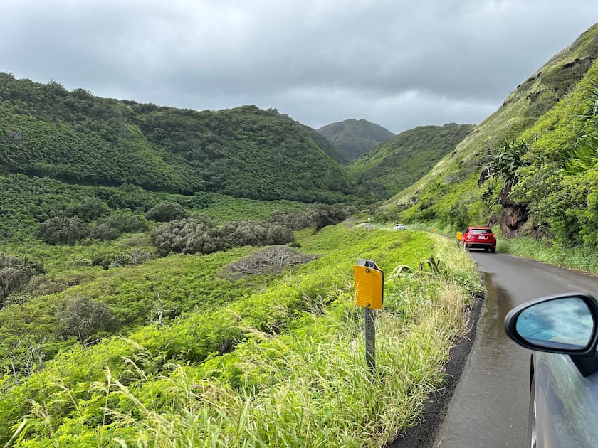 A narrow paved road winds through lush green hills under a cloudy sky, with cars driving along and dense vegetation on both sides—a perfect scene for your 3 Days in Maui Itinerary.