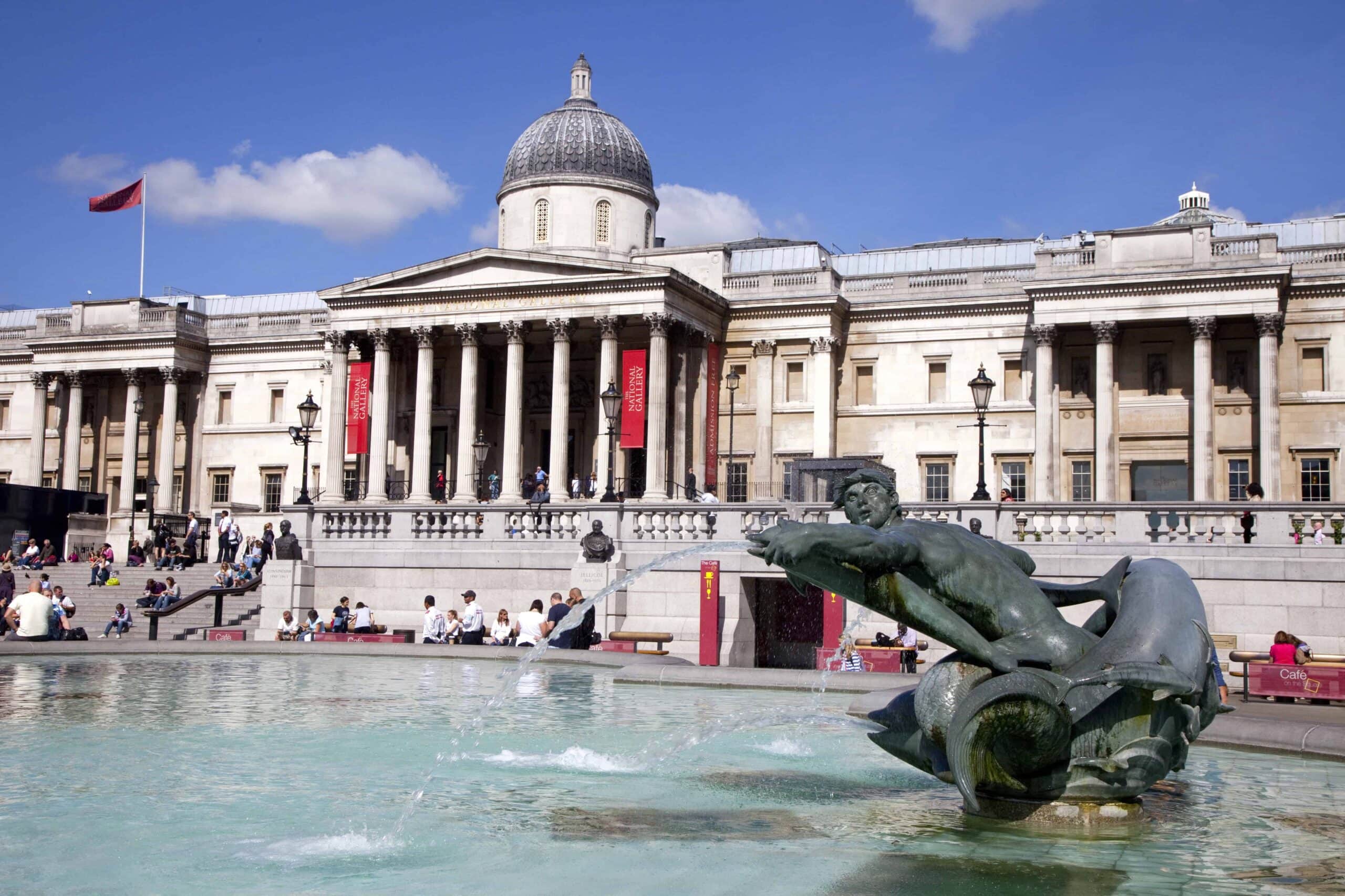 The photo shows the National Gallery in London, one of the top London Museums that are Free, behind a fountain with a bronze merman statue, under a clear blue sky.