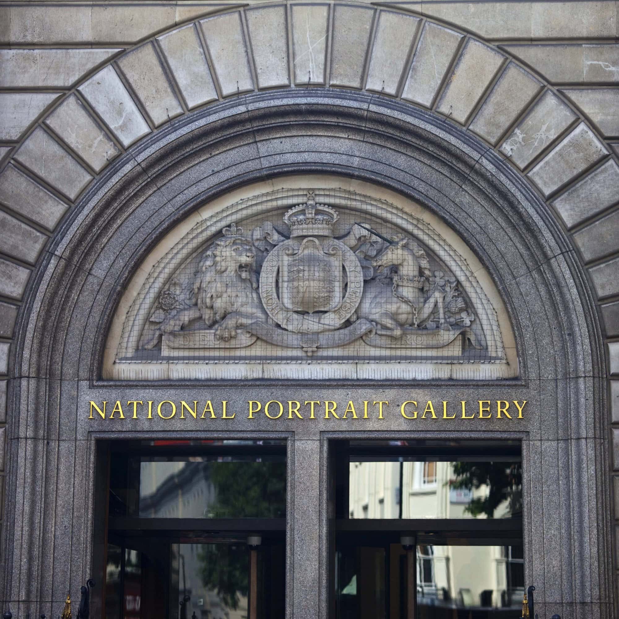 Stone arch entrance of the National Portrait Gallery, one of the London museums that are free, with a sculpted crest featuring a lion, unicorn, and shield above the doorway.