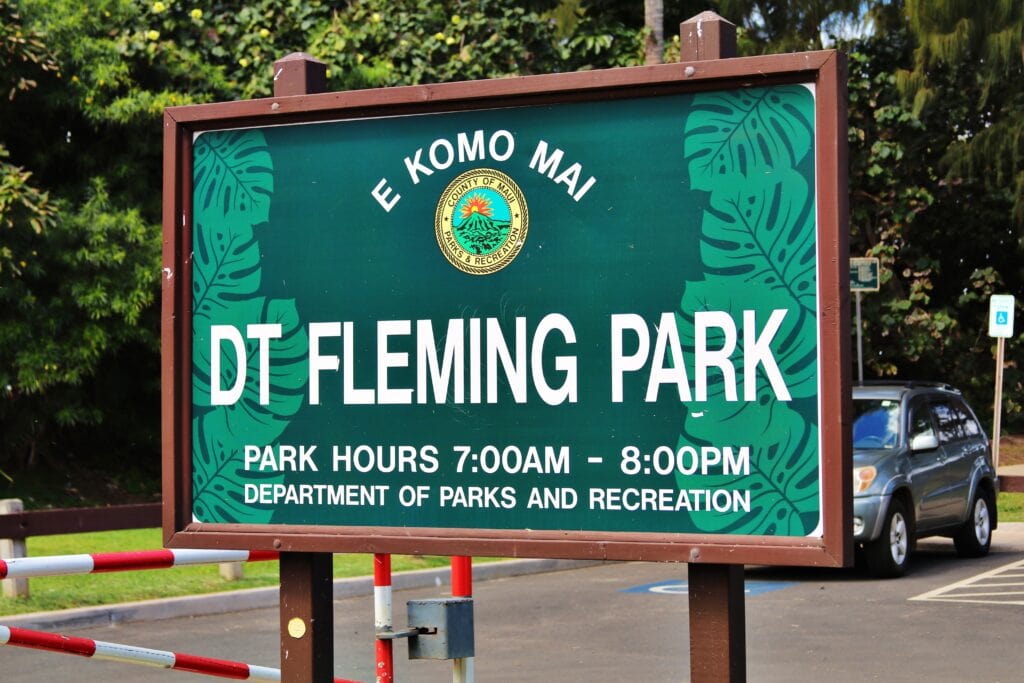 Green sign for DT Fleming Park with park hours 7:00 AM to 8:00 PM, managed by the Department of Parks and Recreation, located in a parking lot near popular DT Fleming Beach snorkeling spots.