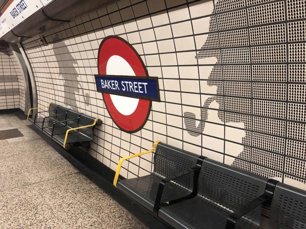 Baker Street London Underground platform with tiled wall art, benches, and the roundel sign.