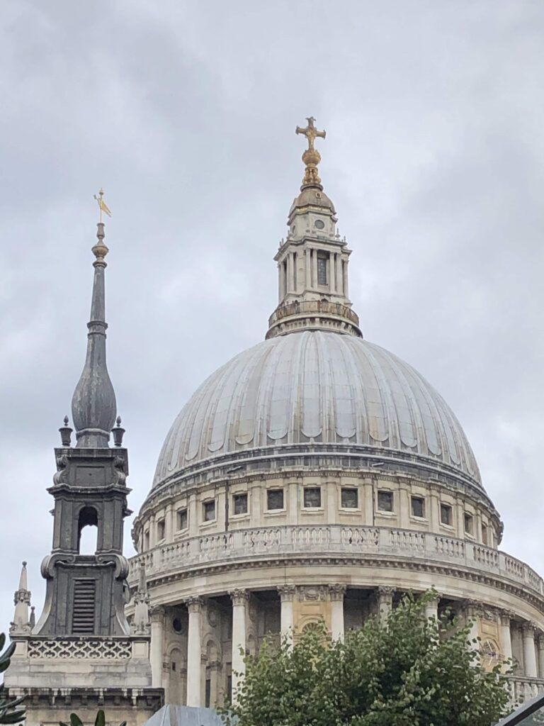 A large domed cathedral with a smaller spire beside it, topped with crosses, under a cloudy sky.