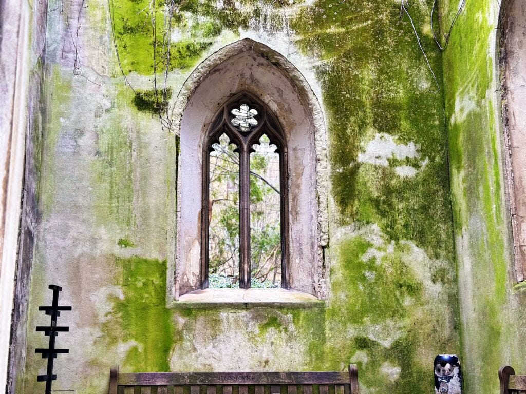 A tall arched window in a weathered, moss-covered stone wall, with a wooden bench below and an urn in the corner—evoking hidden gems among London things to do for free.