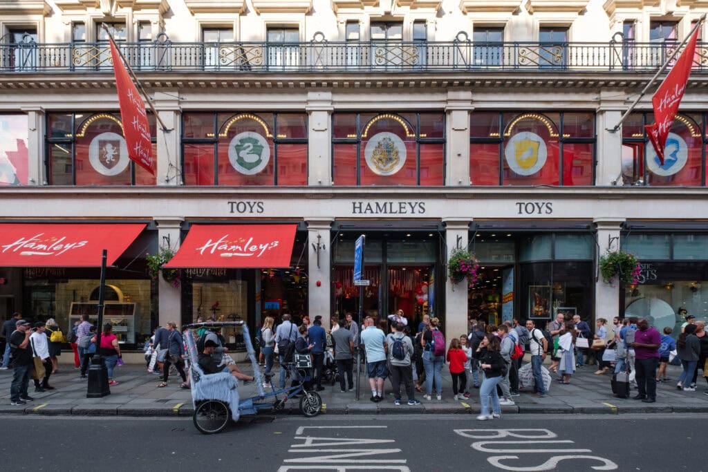 Crowds gather outside the Hamleys toy store in London, with red awnings, flags, and large windows displaying colorful banners above the entrance—a classic stop among London things to do for free.