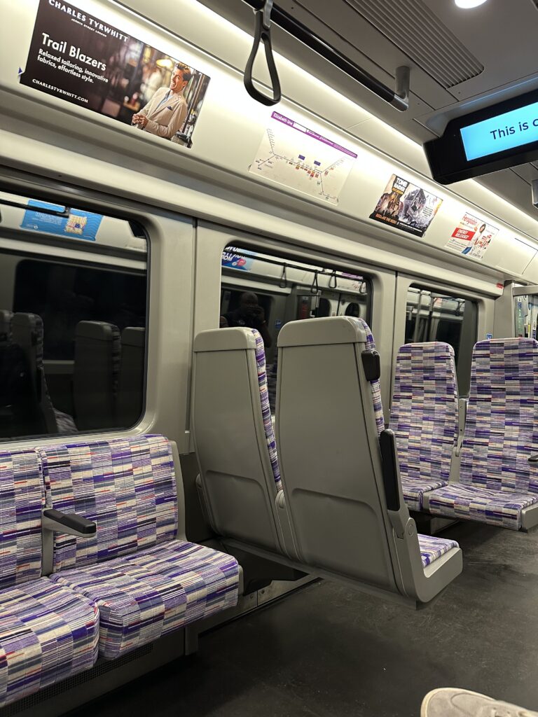 Empty train seats with patterned upholstery, overhead advertisements, and window reflections evoke the quiet moments when learning how to use London Tube trains on a modern night journey.