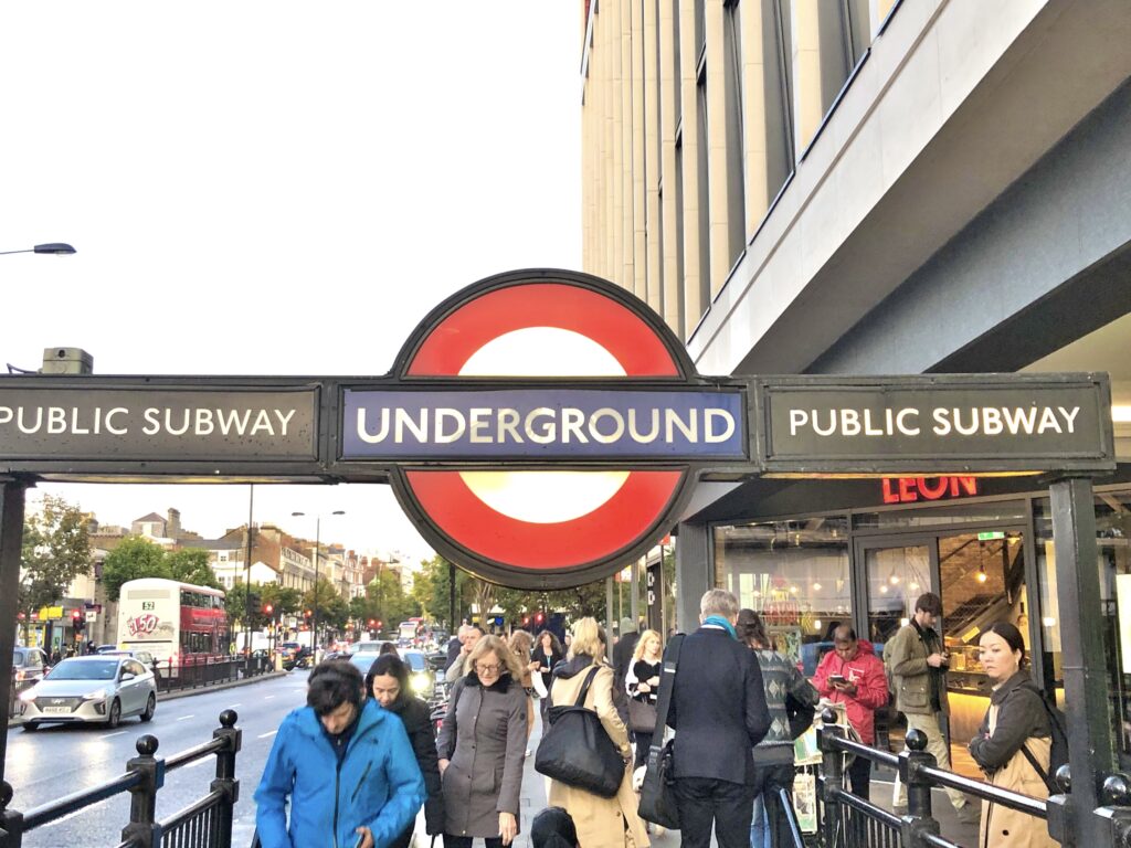 Entrance to a London Underground station with people walking outside, featuring the red and blue "Underground" sign and "Public Subway" text on both sides—a common sight for anyone learning how to use London Tube transport.