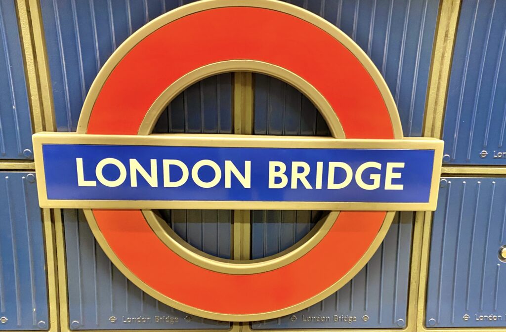 The London Underground roundel sign for London Bridge station is displayed against a blue wall with horizontal lines, offering a classic introduction for those learning how to use London Tube services efficiently.