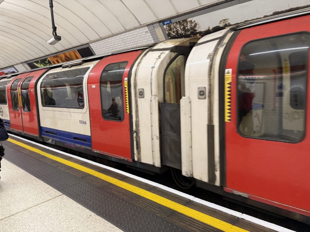 A red and white London Underground train stopped at a well-lit station platform, with doors open and a few passengers visible inside—perfect for those learning how to use London Tube for the first time.